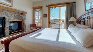Ein Hotelzimmer mit Kamin aus Stein, einem Bett, einem Fernseher, einem Balkon mit Aussicht und einem Holz-Kopfstück.