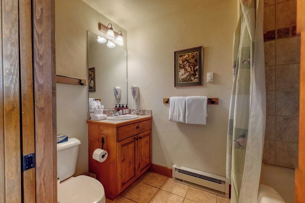 Ein Badezimmer mit Toilette, Waschbecken, Waschtisch, Spiegel, Handtuchhalter und Duschvorhang.