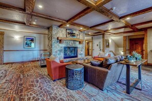 A spacious room with a stone fireplace, a sofa, a round table, and a patterned carpet. - Top-floor, walk-to-lift, corner condo w/ fireplace, views & resort hot tubs/pool (Steamboat Springs)