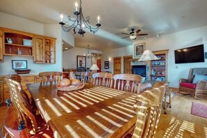 A dining area with a wooden table, chairs, a chandelier, and a fireplace. - Top-floor, walk-to-lift, corner condo w/ fireplace, views & resort hot tubs/pool (Steamboat Springs)