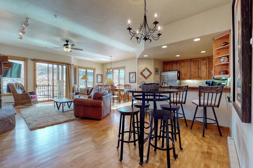 A spacious living area with a dining table, chairs, a sofa, and a kitchen area with wooden cabinets and a refrigerator.