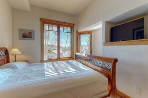 A bedroom with a bed, a TV mounted on the wall, and a window with blinds. - EagleRidge Lodge 308Top-floor, walk-to-lift, corner condo w/ fireplace, views & resort hot tubs/pool (Steamboat Springs)