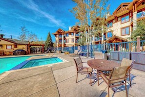 A pool area with a table and chairs, a covered seating area, and a building with multiple balconies. - Top-floor, walk-to-lift, corner condo w/ fireplace, views & resort hot tubs/pool (Steamboat Springs)
