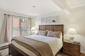 Ein Schlafzimmer mit einem Bett, zwei Nachttischen, einem Fenster mit Jalousien und einem an der Wand hängenden Kunstwerk.