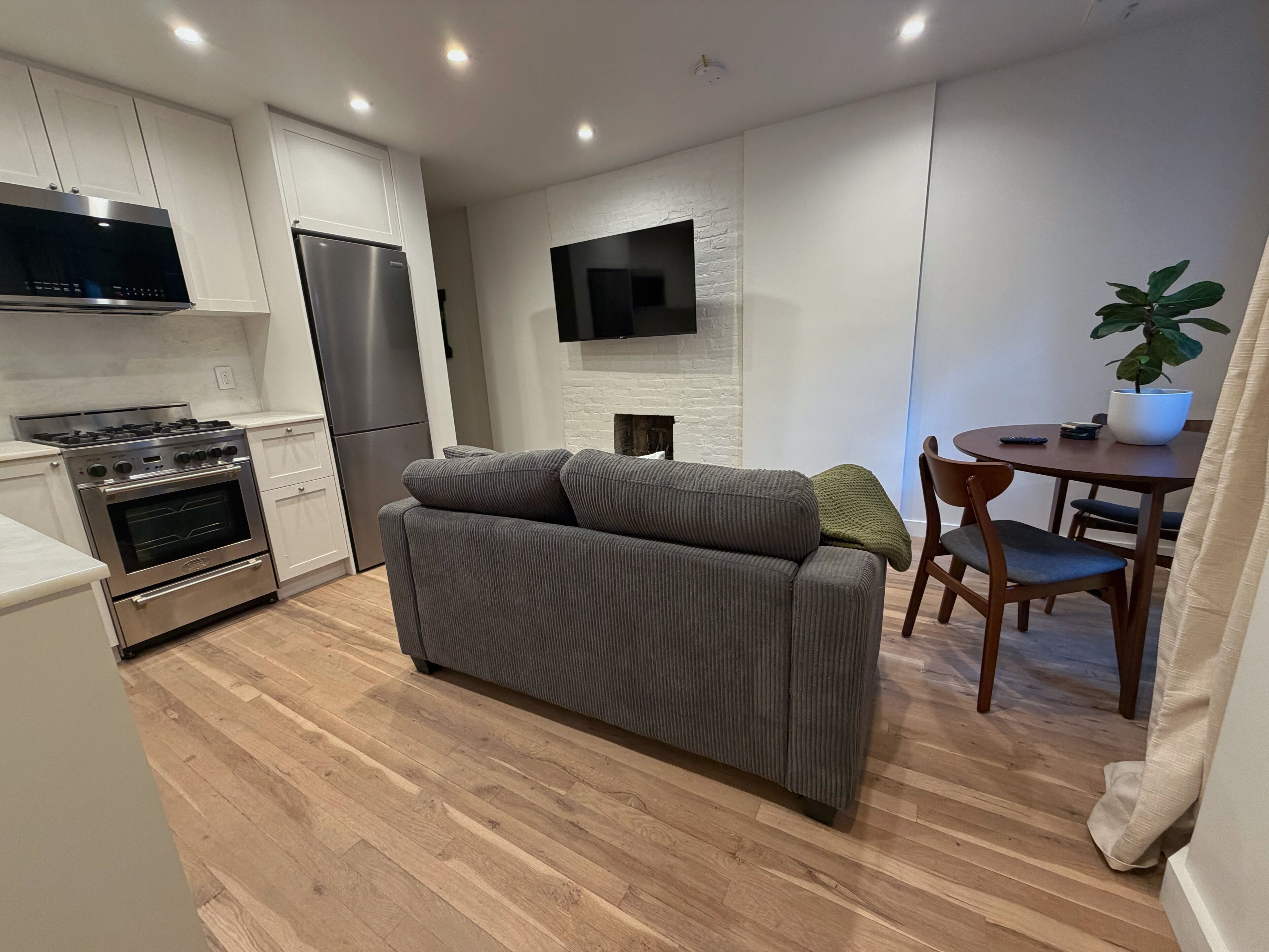 Une cuisine moderne dotée d’appareils électroménagers intégrés, un canapé gris, une table à manger avec des chaises et un téléviseur à écran plat fixé au mur.