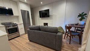 Une cuisine moderne dotée d’appareils électroménagers intégrés, un canapé gris, une table à manger avec des chaises et un téléviseur à écran plat fixé au mur.