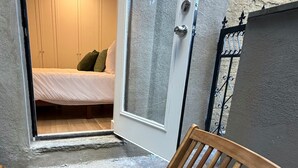Une chaise en bois est placée dans l’embrasure d’une porte qui donne sur une pièce où se trouve un lit et une porte blanche.