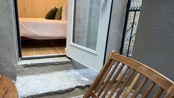 Une chaise en bois est placée dans l’embrasure d’une porte qui donne sur une pièce où se trouve un lit et une porte blanche.