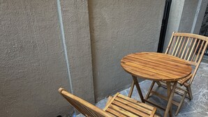 Une table et une chaise en bois, placées devant un mur à texture, avec une grille en métal en arrière-plan.