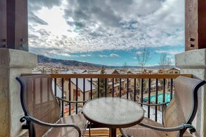 A balcony with two chairs and a table, overlooking a swimming pool and a mountainous landscape. - Top-floor condo w/ gorgeous view, fireplace & resort pool/hot tubs/shuttle/gym (Steamboat Springs)