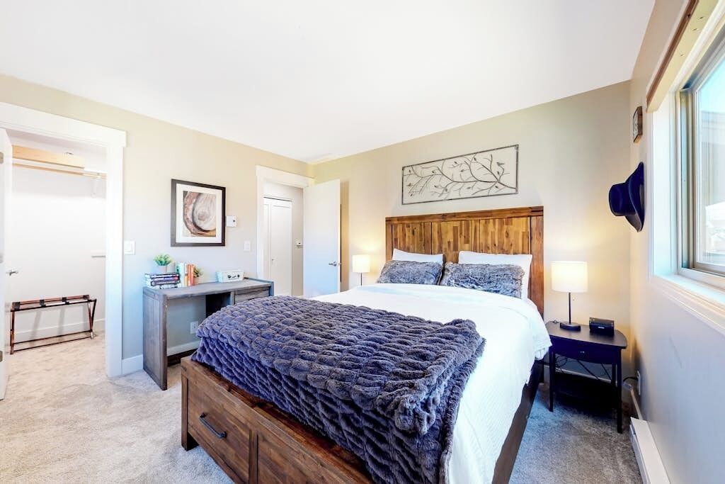 Une chambre à coucher avec un lit, une table de chevet, une lampe et une œuvre d’art accrochée au mur.