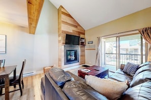 A living room with a fireplace, a sofa, a coffee table, and a dining area. - Updated, Top-Floor Condo w/ Gas Fireplace, Shared Pool/Hot Tub - Walk to Shuttle (Steamboat Springs)