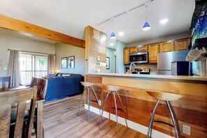 A modern kitchen with wooden accents, a dining area with a blue sofa, and a bar with stools. - Updated, Top-Floor Condo w/ Gas Fireplace, Shared Pool/Hot Tub - Walk to Shuttle (Steamboat Springs)