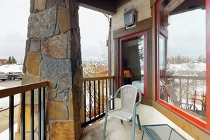 A stone exterior wall, a balcony with a chair, and a view of a snowy landscape. - Walk-to-lift condo w/ fireplace, W/D, WiFi & shared hot tubs/pool/ski shuttle (Steamboat Springs)