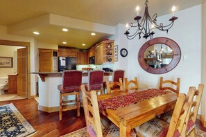 A dining area with a wooden table and chairs, a chandelier, and a round mirror on the wall. - Walk-to-lift condo w/ fireplace, W/D, WiFi & shared hot tubs/pool/ski shuttle (Steamboat Springs)