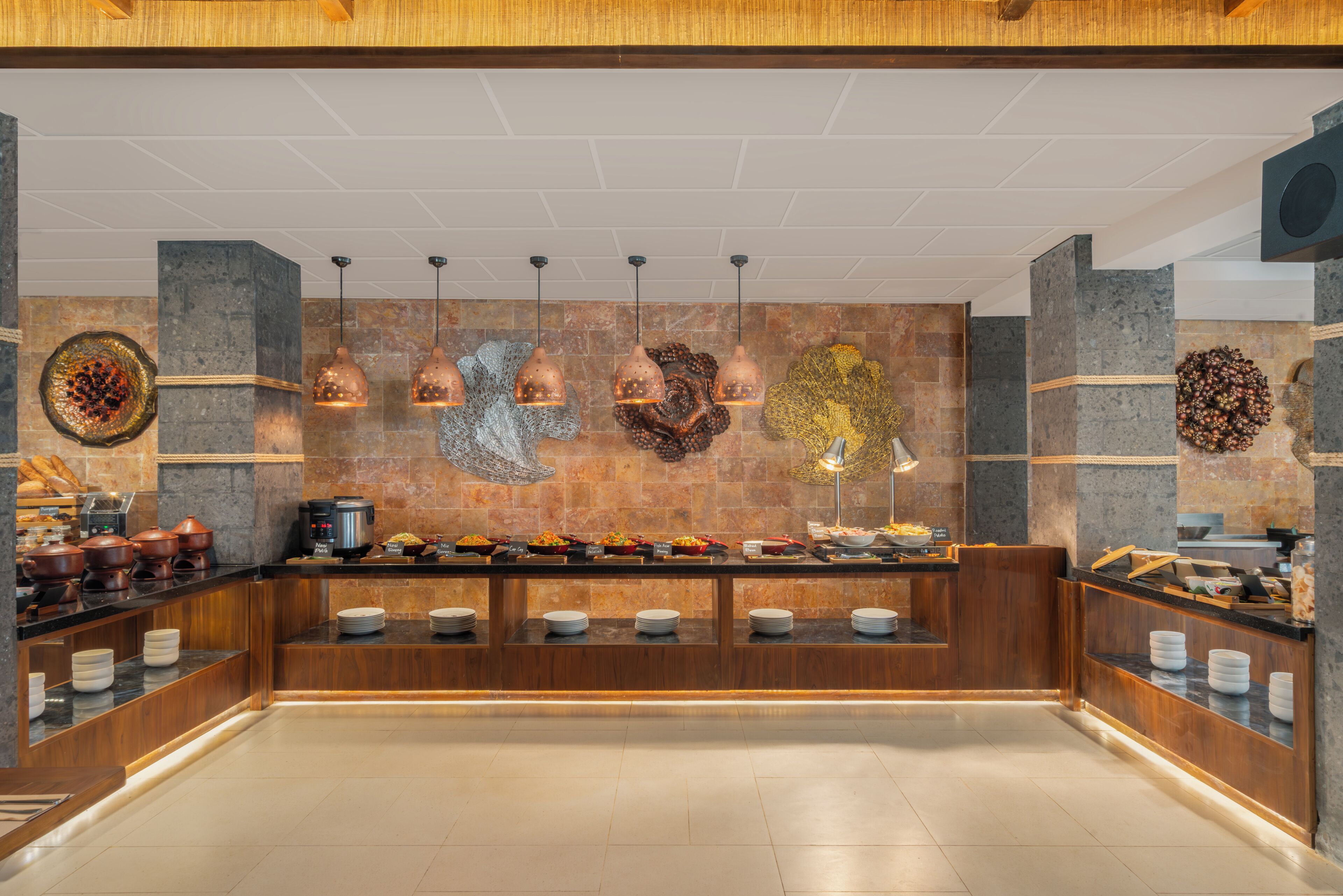 Zona de buffet amb una gran varietat d'aliments, una barra llarga i llums penjants.