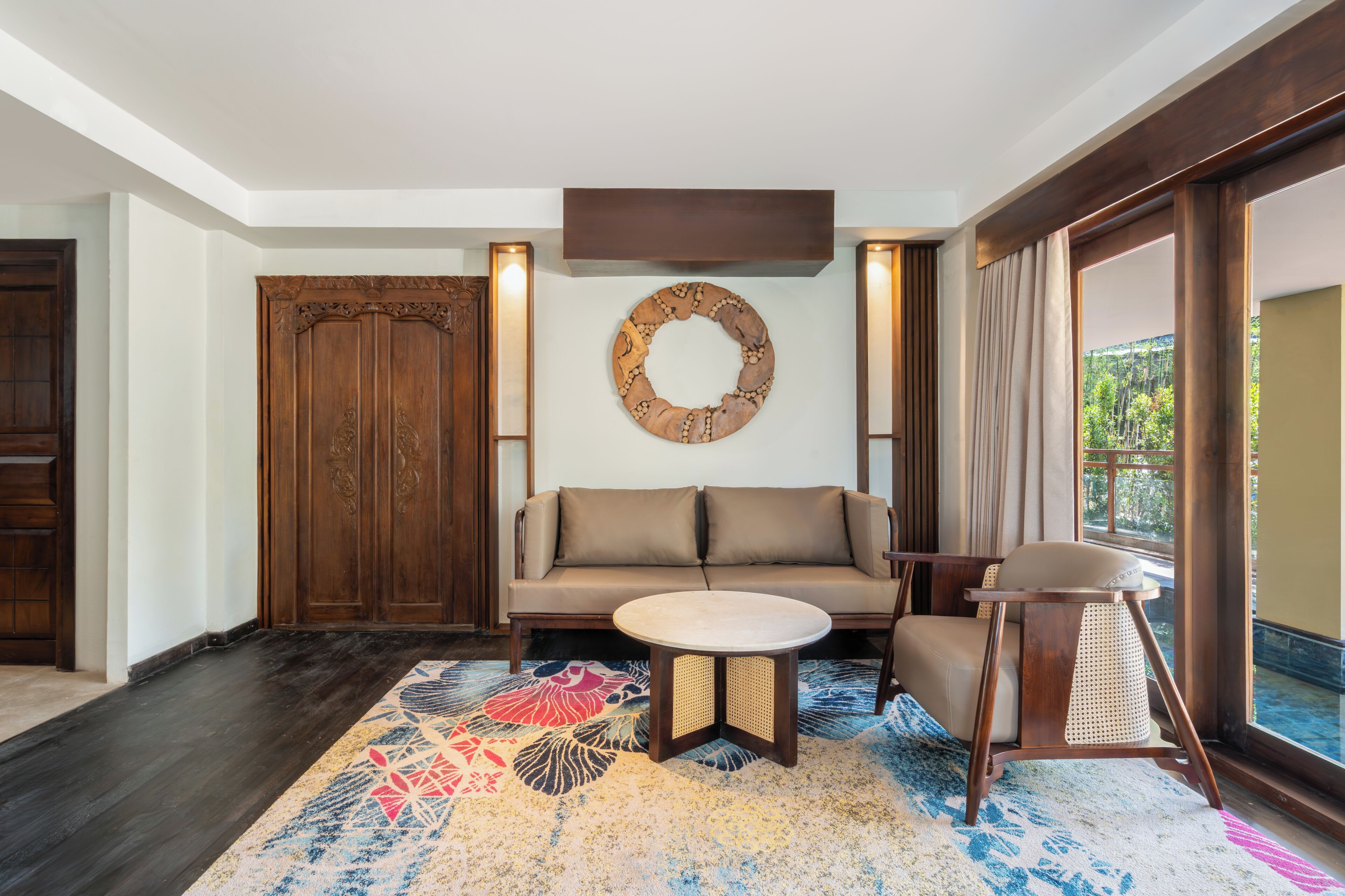 A room with a sofa, a round table, a decorative wall piece, and a view through a window.