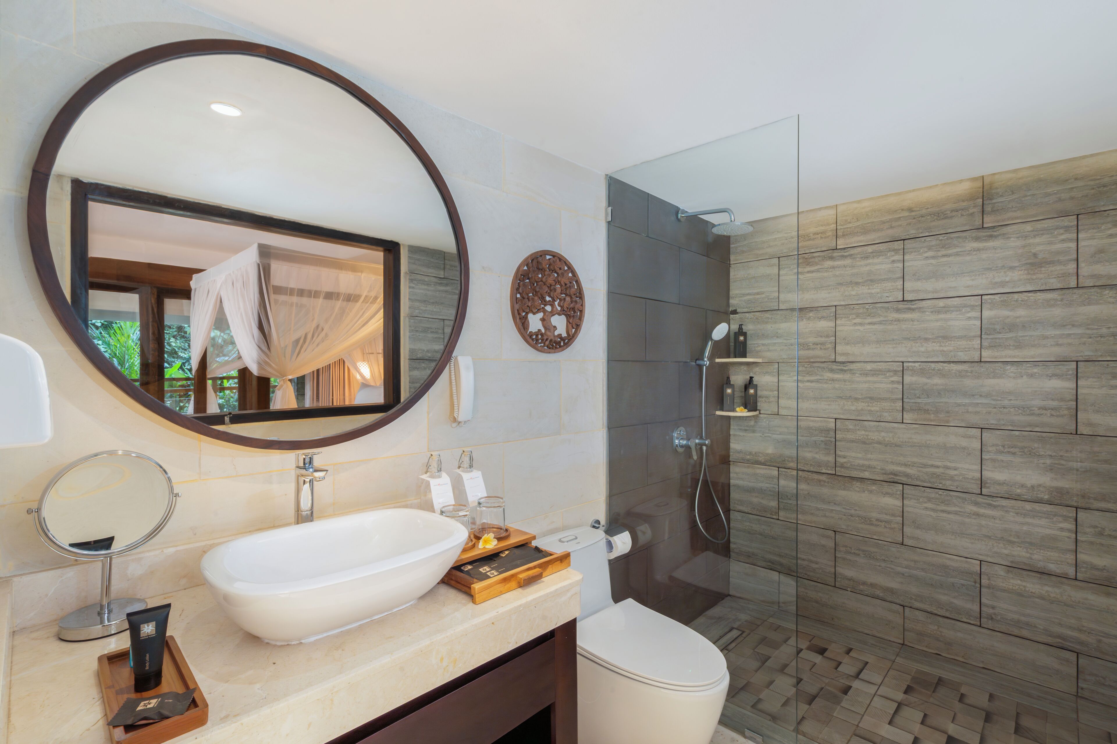 A modern bathroom with a large oval mirror, a white sink, a glass shower enclosure, and a wooden vanity.