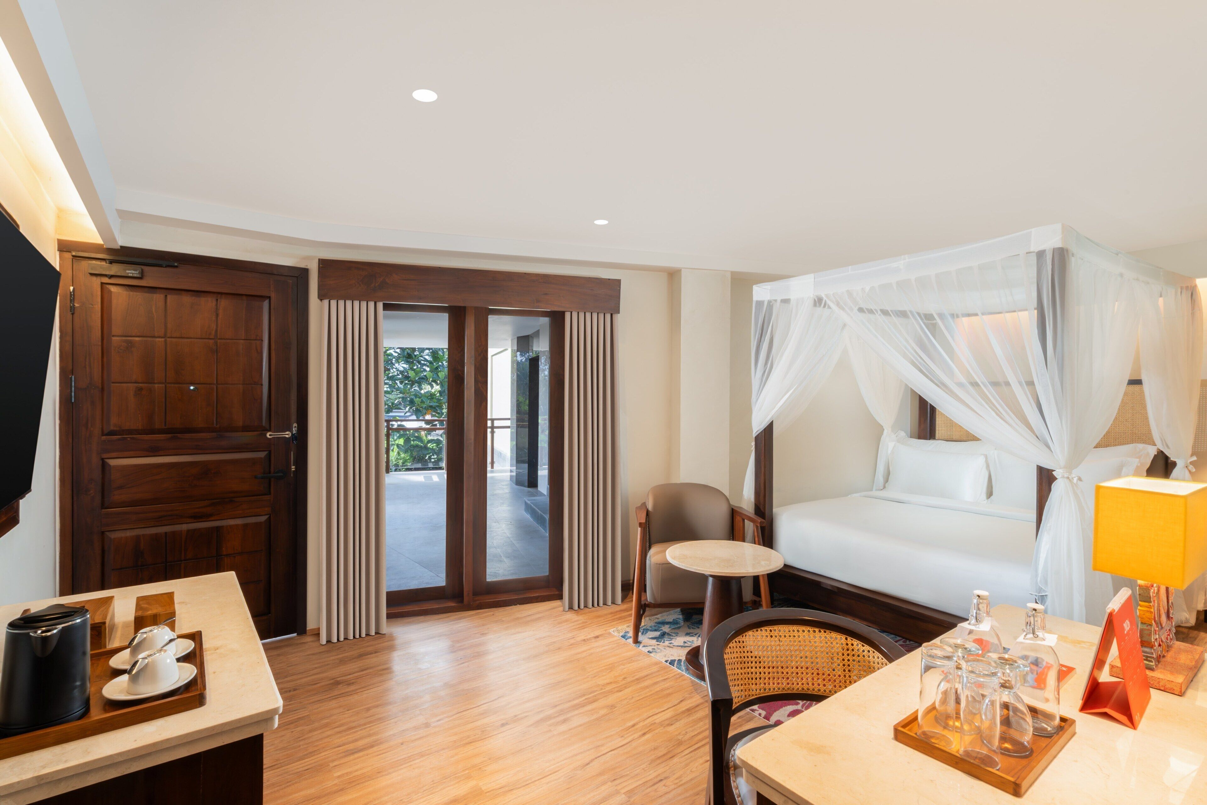 A hotel room with a bed, a table with a tray of items, a chair, and a view of the outdoors.