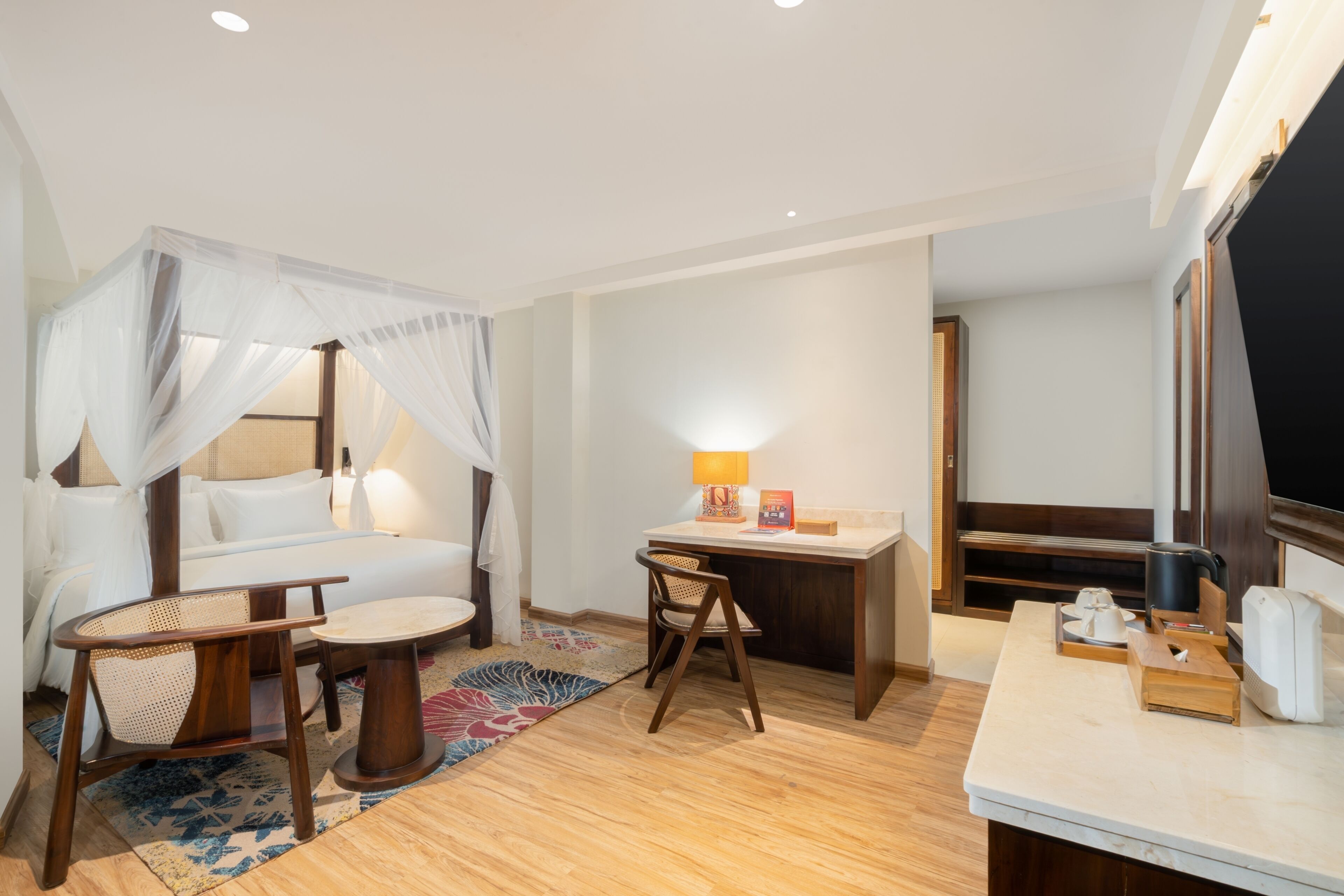 A hotel room with a bed, a desk, a chair, a small table, a TV, and a window.