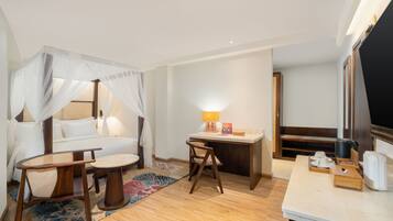 A hotel room with a bed, a desk, a chair, a small table, a TV, and a window.
