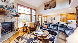 A spacious living room with a fireplace, a large sofa, a coffee table, and a dining area with wooden cabinets. - 1410 EagleRidge Multi-level townhome with AC, fireplace, pool & hot tubs - walk to the gondola (Steamboat Springs)