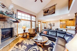 A spacious living room with a fireplace, a large sofa, a coffee table, and a dining area with wooden cabinets. - Multi-level townhome with AC, fireplace, pool & hot tubs - walk to the gondola (Steamboat Springs)