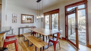 Una cocina con una mesa de madera y bancos, un espejo grande y una puerta corrediza de vidrio que da a una terraza al aire libre.