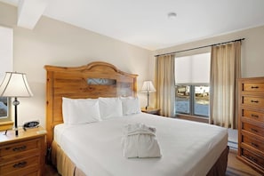 Ein Hotelzimmer mit einem hölzernen Kopfteil, einem ordentlich bezogenen Bett, einem Schminktisch und einem Fenster mit Vorhängen.
