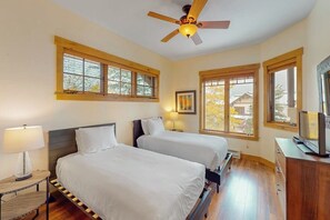 A bedroom with two beds, a ceiling fan, large windows, a TV, and a dresser. - Walk-to-lift condo w/ shared hot tubs/pool/gym & amazing mountain views (Steamboat Springs)