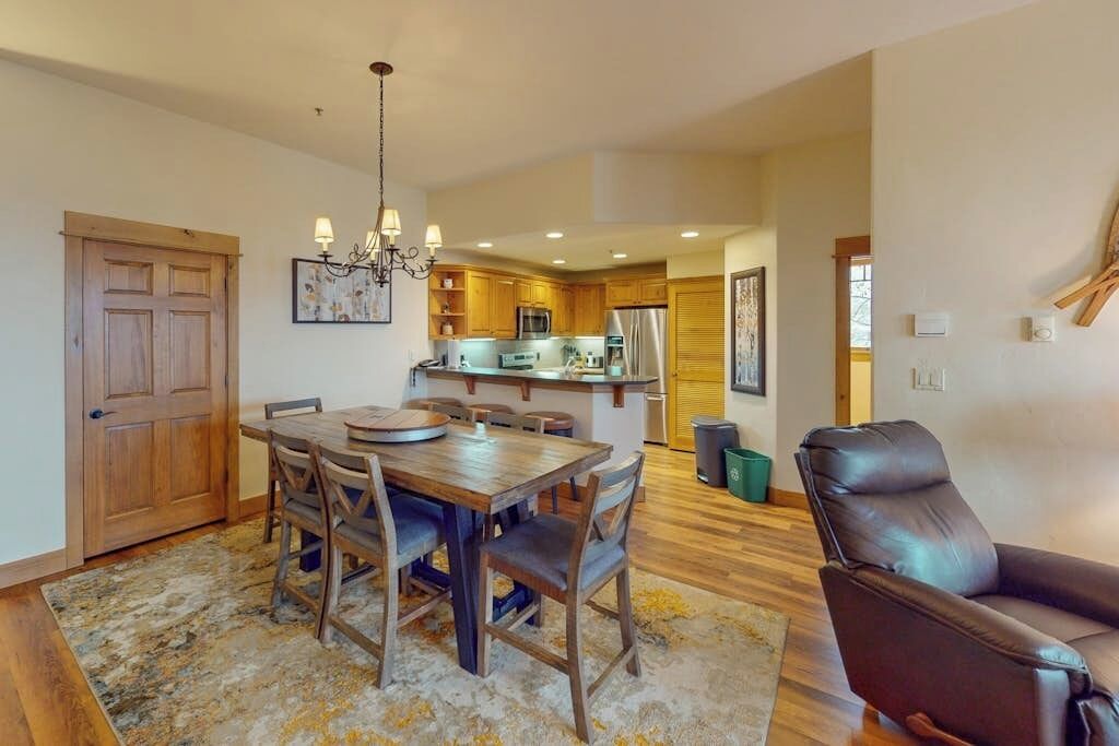 Comedor con una mesa y sillas de madera, un candelabro y una cocina al fondo.
