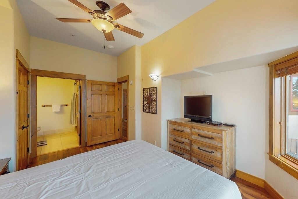 A bedroom with a bed, wooden wardrobe, ceiling fan, and a television on a dresser.
