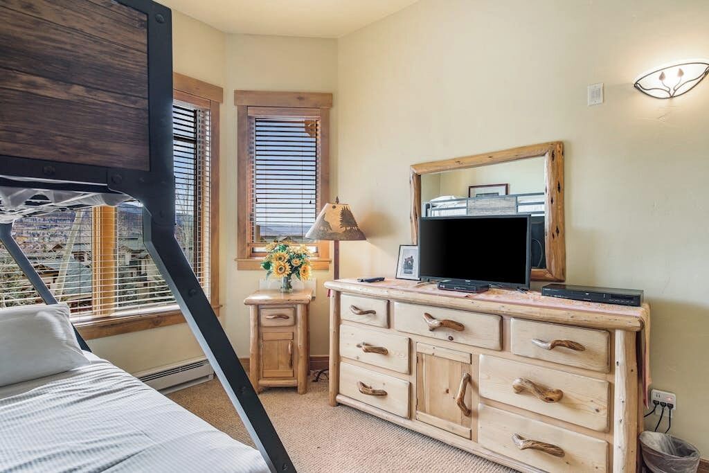 A bedroom with a bed, a dresser, a TV, and a window with blinds.