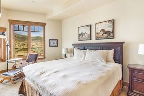Ein Schlafzimmer mit einem großen Bett, einem Sessel, einem Schreibtisch und einem Fenster mit Jalousien.