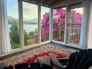 Una habitación con un ventanal grande, una alfombra estampada y una silla.