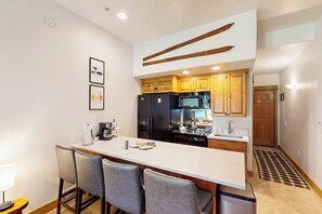 A modern kitchen with a central island, bar stools, wooden cabinets, and a black refrigerator. - Walk-to-gondola studio with hot tubs, pool, fitness room, and ski shuttle (Steamboat Springs)