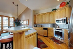 A kitchen with wooden cabinets, a microwave, an oven, a sink, and a bar area with stools. - Pretty & bright townhome in a great location for skiing w/ shared hot tubs (Steamboat Springs)