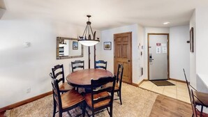 A dining area with a round table, chairs, a chandelier, and a wooden door. - Timber Run 313 - Lovable condo with pool, hot tubs, sauna & clubhouse (Steamboat Springs)