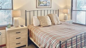 A neatly made bed with a striped bedspread, two bedside lamps, a nightstand with drawers, and a framed picture on the wall. - Timber Run 313 - Lovable condo with pool, hot tubs, sauna & clubhouse (Steamboat Springs)
