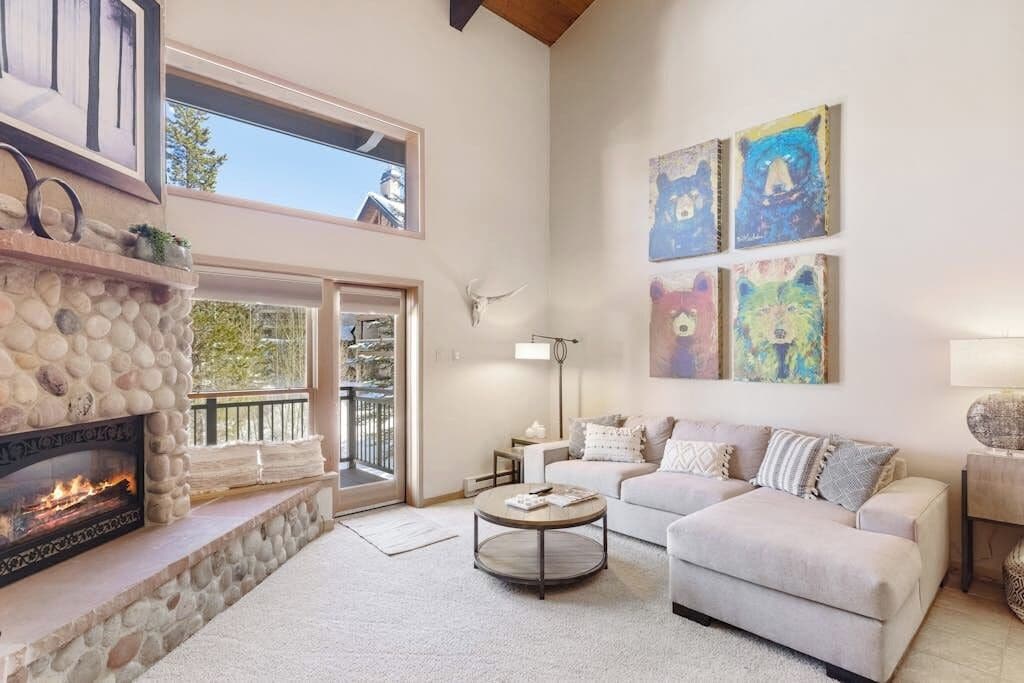 A spacious living room with a stone fireplace, a large couch, a coffee table, and artwork on the walls.