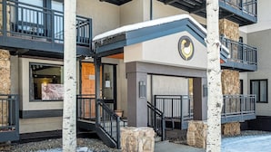 Un immeuble à plusieurs étages, doté d’une façade en pierre, d’une entrée enneigée et d’un balcon avec une rambarde en métal.