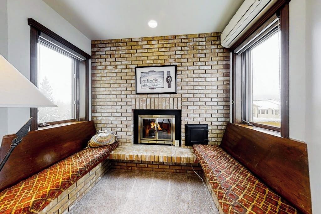 A room with a brick wall, a fireplace, a bench, and a window.