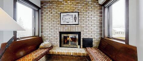 A room with a brick wall, a fireplace, a bench, and a window.