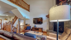 Ein großzügiger Wohnbereich mit Kamin, Ledersofas, Fernseher und einer Treppe.