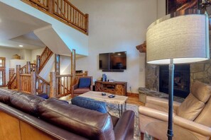 Ein großzügiger Wohnbereich mit Kamin, Ledersofas, Fernseher und einer Treppe.