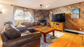 Een woonkamer met een leren bank, een houten salontafel, een flatscreen-televisie, een stenen openhaard en een houten wandpaneel.