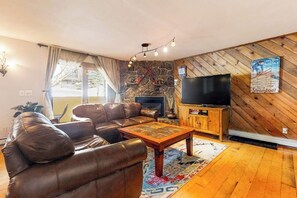Ein Wohnzimmer mit einer Ledersofa, einem Holztisch, einem Flachbildfernseher, einem Kamin aus Stein und einer Holzvertäfelung.
