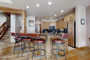 A kitchen with wooden cabinets, a central island with bar stools, and a staircase leading to another level. - 1516 EagleRidge Walk-to-gondola townhome w/ private hot tub & resort pool/firepit/hot tubs (Steamboat Springs)