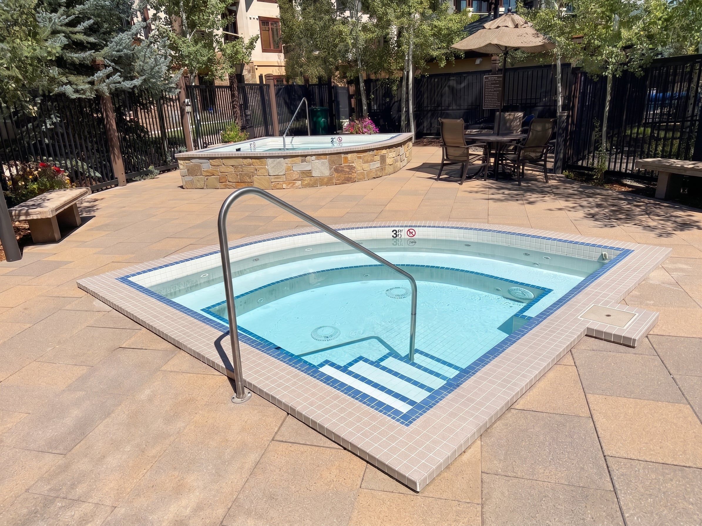 Une piscine rectangulaire bordée de carreaux, avec un escalier en métal et un mur de pierre en arrière-plan.