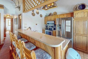 Eine Küche mit Holzausstattung, einem Edelstahl-Kühlschrank, einer Mikrowelle und einer Bar mit Holzstühlen.